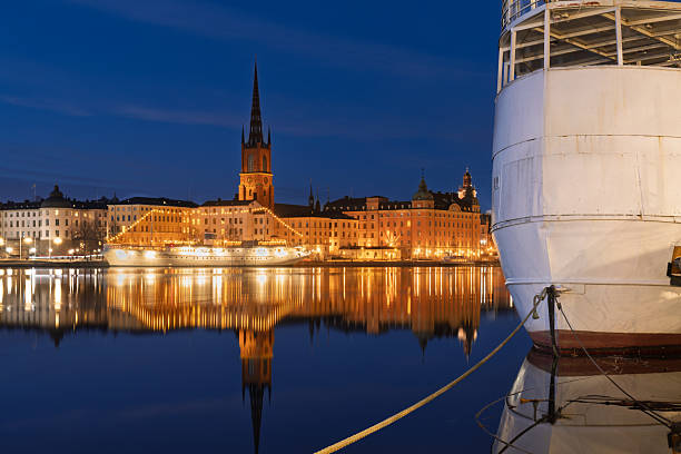 A stunning nighttime view of Stockholm, Sweden, with city lights reflecting on the calm water, featuring historic architecture and the illuminated skyline.