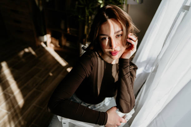 istock Young woman posing while sitting near window with sunlight on face 2206613999