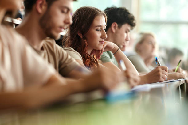 istock Young female student and her friends writing on a class in lecture hall. 2206616003