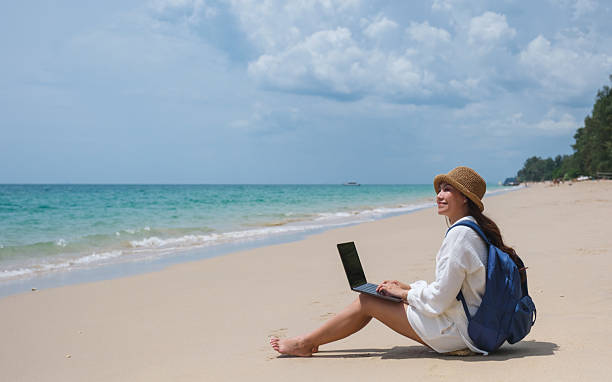 istock A female traveler using and working on laptop computer while sitting on the beach 2206617886