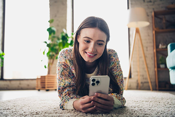 istock Young woman relaxing at home, lying on the floor while using her smartphone, in a cozy daylight-filled interior setting 2206618733