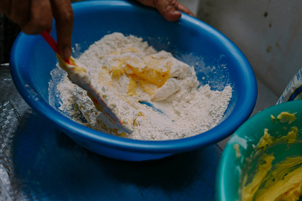 A person preparing dough for cookies in a blue plastic bowl. Baking ingredients are mixed by hand using a whisk. Shot inside, close-up, nobody in the frame. Culinary food preparation concept