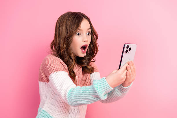 驚いた若い女の子がスマートフォンを持ち、ピンクの背景に驚きを表現しています - 驚く ストックフォトと画像