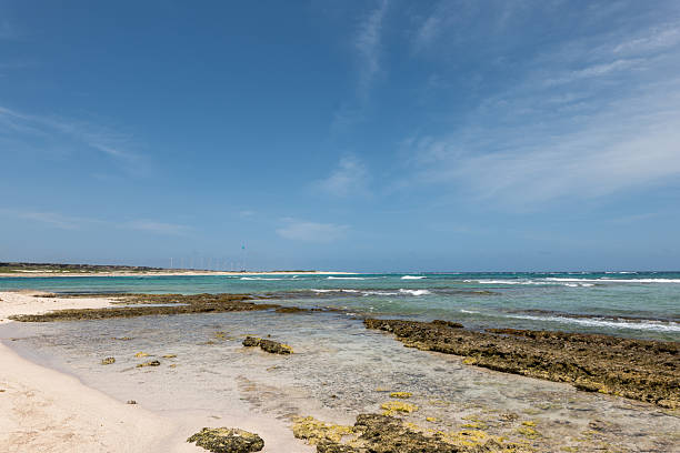 Clear waters meet sandy shores on a calm, sunny day. Rocky coastline stretches into the horizon. Ideal for travel, nature, and relaxation themes.