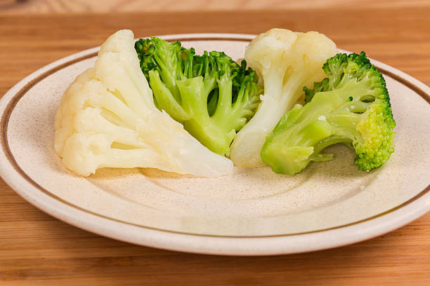 Several small pieces of freshly boiled broccoli and cauliflower on the saucer on wooden surface, front view close-up in selective focus