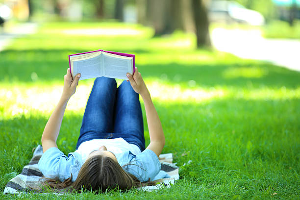 istock Cute girl lying with book in the park 2206636627
