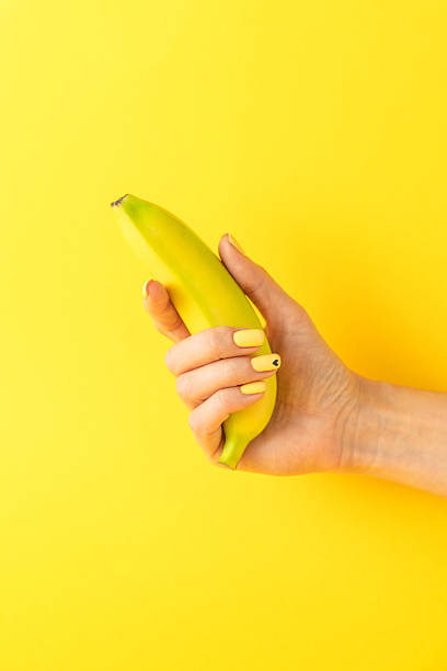 istock Hand holding banana with bright yellow background for playful fruit-themed concept 2206639849