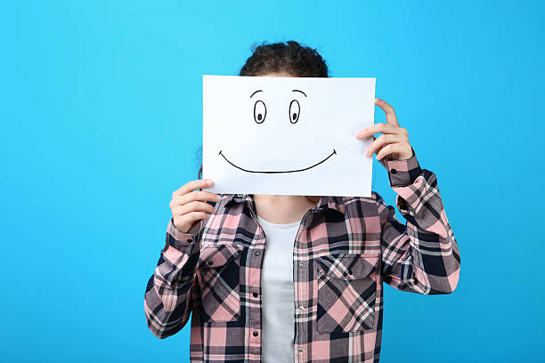 istock Girl holding paper with drawing face on blue background 2206645171