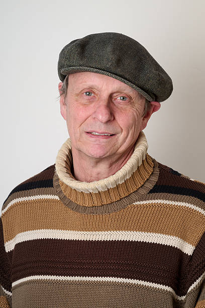 Senior man with a beige turtleneck puulover and a vintage cap on head against white wall