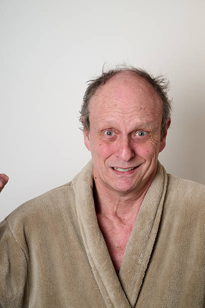 Old man beige bathrobe and tousled hair make a ugly face in front of camera