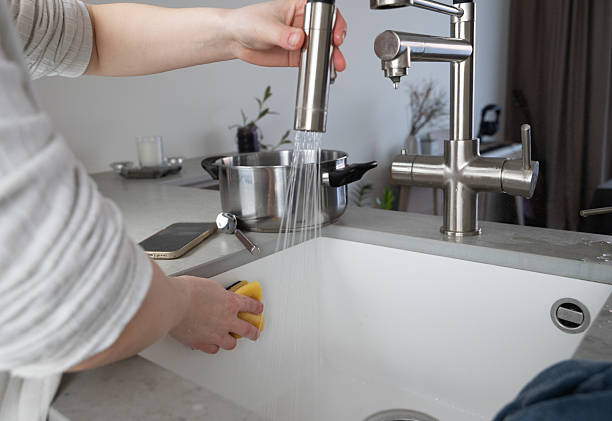 Hands are cleaning a kitchen sink using fresh water to ensure everything is spotless and tidy A person diligently washes a kitchen sink with a sponge while water flows smoothly from a modern faucet water sanitation worker washing faucet stock pictures, royalty-free photos & images