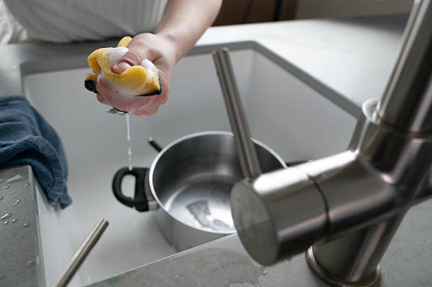 Washing Dishes by Hand Using a Sponge in a Contemporary Kitchen Area with Modern Appliances A person is diligently washing dishes using a bright yellow sponge in a stylish kitchen sink that looks modern water sanitation worker washing faucet stock pictures, royalty-free photos & images