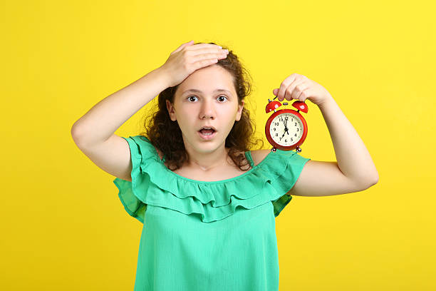 istock Young girl holding clock on yellow background 2206649231
