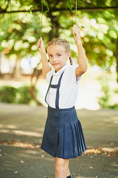 Portrait of a smiling elementary school girl enjoying her leisure time in a park, playing with hanging branches and soaking up the joy of childhood after class