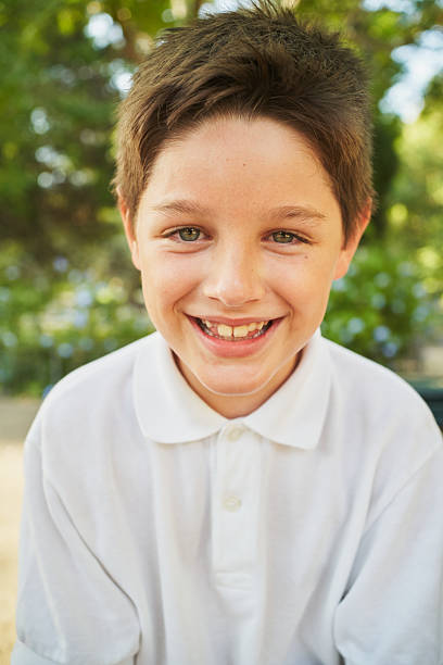 Portrait of a cheerful elementary age boy wearing a school uniform, smiling brightly at the camera in a sunny outdoor setting, possibly during recess or after school