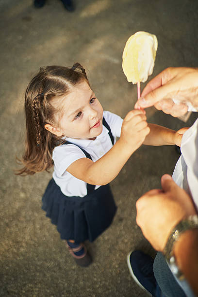 Preschool girl in a school uniform happily receiving a colorful lollipop from her teacher during a joyful break time in the schoolyard, enjoying a sweet treat together