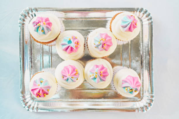 Eight cupcakes decorated with pink and blue meringue swirls and gold sprinkles are neatly arranged on a silver tray, ready to be enjoyed at a party or celebration