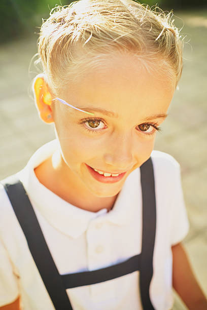 Portrait of a cheerful elementary schoolgirl smiling brightly at the camera, enjoying a sunny day in the schoolyard, radiating happiness with her blond braids and green eyes