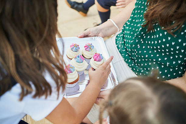 Elementary age students are choosing delicious cupcakes from a tray held by a teacher during school break time, enjoying a sweet treat together