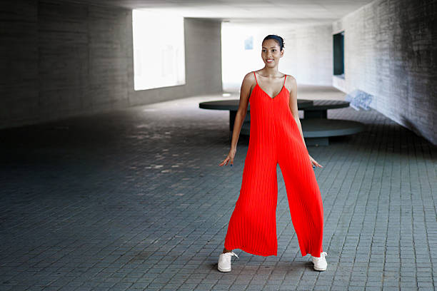 A fashionable and stylish woman stands confidently in a vibrant, eyecatching red jumpsuit, showcasing contemporary fashion trends amidst a lively urban setting with energy all around her