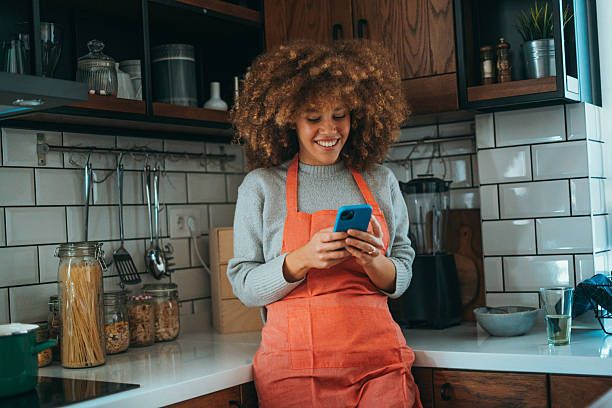 istock A young woman with natural curls, leaning on the kitchen counter, wearing a cooking apron, using her phone, radiates relaxed energy. 2206657558
