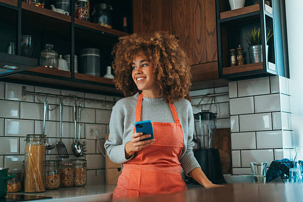 istock A young woman with natural curls, leaning on the kitchen counter, wearing a cooking apron, using her phone, radiates relaxed energy. 2206658248