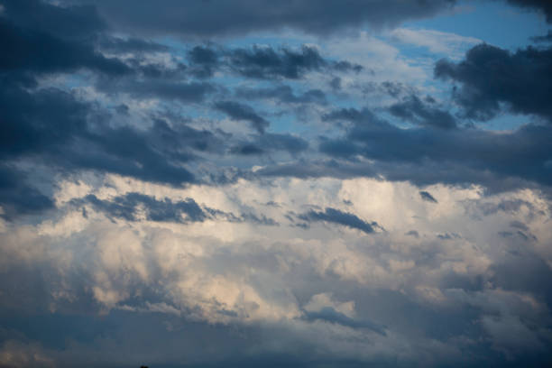 A captivating sky displays an array of clouds in various shades of gray and white. Sunlight breaks through, creating a dynamic interplay of light and shadow around the clouds. This scene evokes a sense of tranquility and wonder.