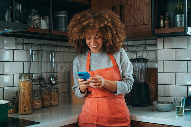 istock A young woman with natural curls, leaning on the kitchen counter, wearing a cooking apron, using her phone, radiates relaxed energy. 2206659683