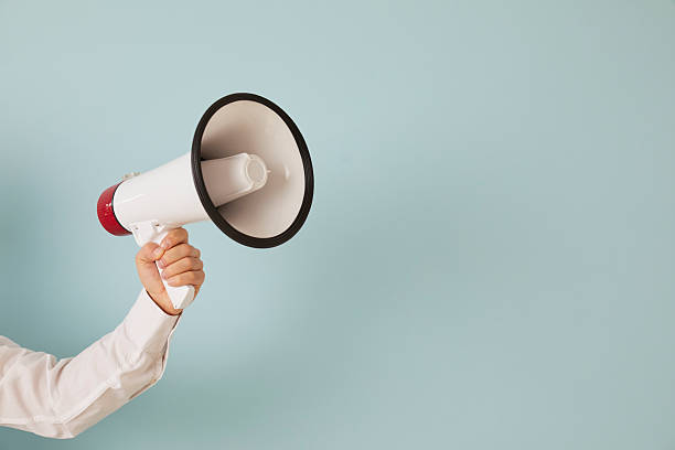 Hand of an unknown man holds loudspeaker which is symbol of advertising, PR and promotion. stock photo