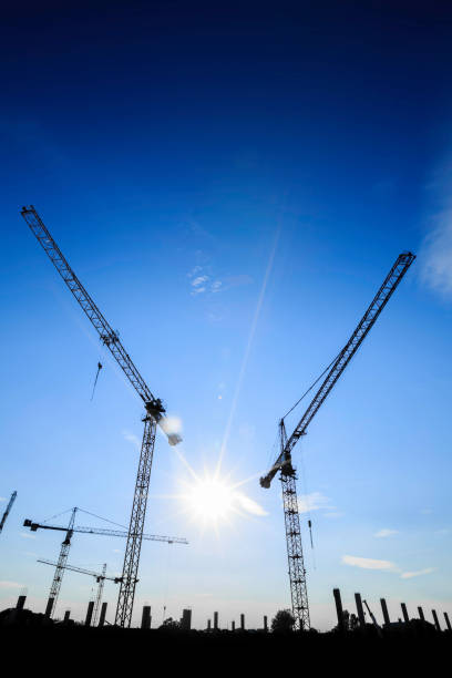 istock Construction cranes silhouetted against a bright blue sky during sunset with the sun illuminating the scene 2206666209