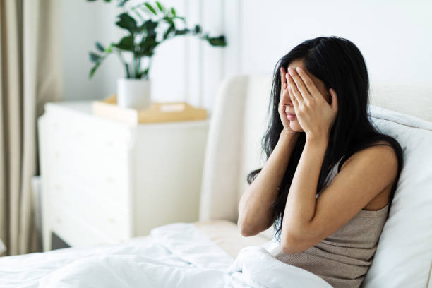 istock Depressed woman sitting in bed hiding head in hands 2206667463
