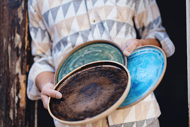 Artisan showcasing beautiful handmade ceramic plates, featuring intricate designs in vibrant green, blue, and brown hues, reflecting high craftsmanship and artistic dedication.