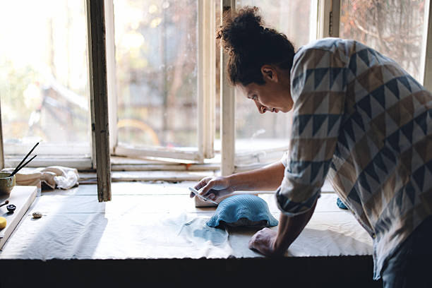 Creative female artist paints with oil on canvas, standing near easel with brush. Focused woman creating picture, making artwork at home. Inspired girl at workshop doing art with acrylic paints.