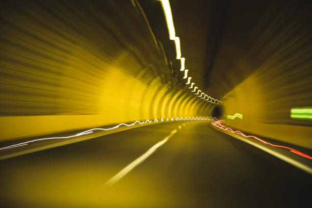 A vehicle speeds through a uniquely illuminated tunnel, showcasing vibrant yellow lights and dynamic motion blur. The smooth drive reveals the curving road ahead, creating an exciting nighttime journey.