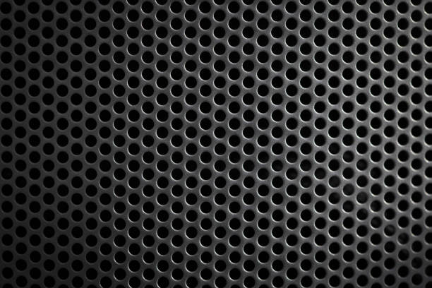 Close-up view of a metallic mesh featuring numerous circular holes arranged in a precise pattern. The surface showcases a modern industrial design, highlighting shadows and reflections that enhance the visual appeal.