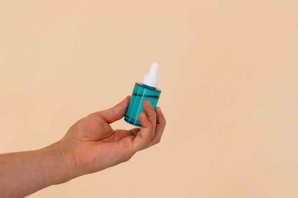 istock Hand holding blue serum dropper bottle on peach background with ample copy space 2206680809