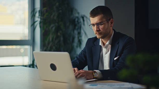 istock Focused businessman in a suit working on a laptop in a modern office environment. Serious, concentrated expression suggests deep thought and analysis. Productivity, corporate work, business strategy 2206682448