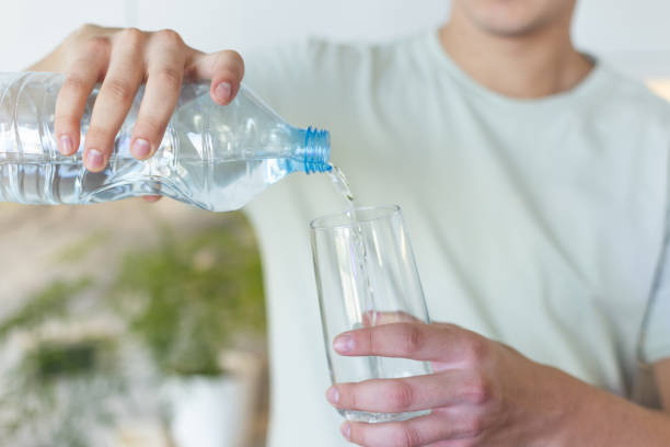 istock Young Man Pouring Water from Plastic Bottle Into Glass in Kitchen Environment 2206682778