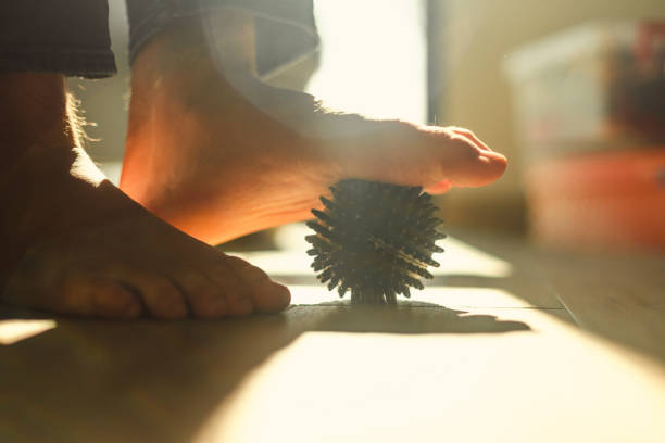Close-up of a person massaging their foot with a spiky ball, promoting relaxation and wellness. The sunlight enhances the ambient and natural appeal of this reflexology or therapeutic technique.