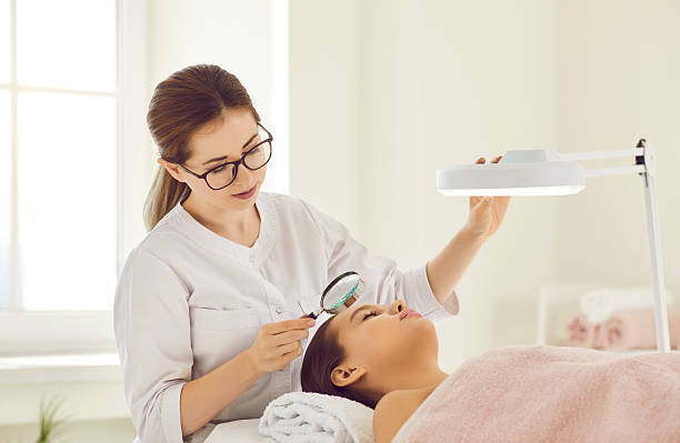 istock Female beautician holding small magnifying glass looking through it examining condition of skin. 2206686880