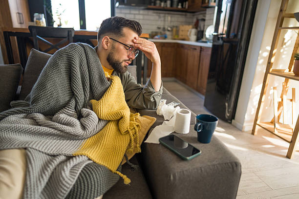 istock Sick young man suffering from cold or flu sitting on sofa covered with blanket 2206688955