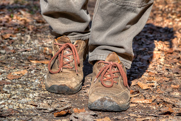 A man walks along a leaf-covered path wearing sturdy hiking boots, providing support and comfort on his adventure through nature.