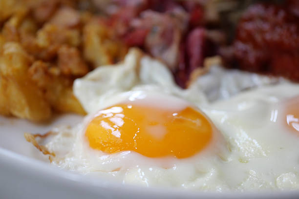 A closeup of perfectly fried eggs on a plate with bacon and toast as breakfast sides