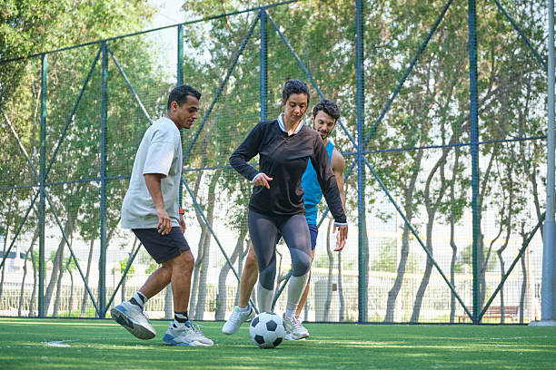 Woman kicking ball while playing soccer with men. Male defense players are defending. They are at turf.