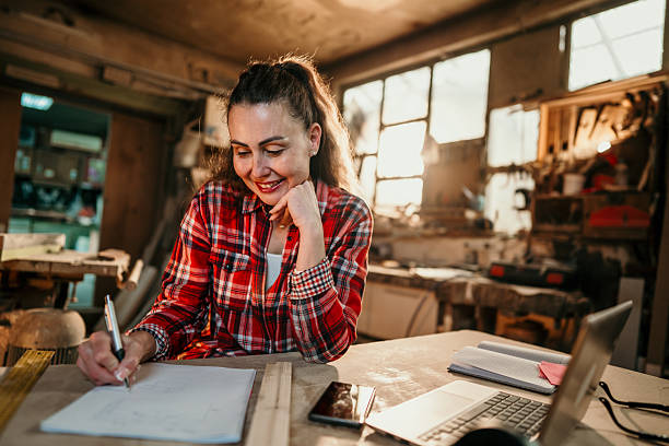 istock Female carpenter designing furniture in workshop using laptop and notebook 2206693539