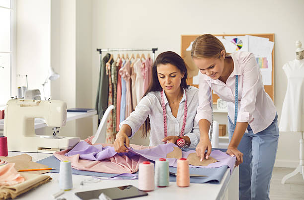 istock Two seamstresses in sewing workshop discuss fabric, pattern and sketch during production process. 2206694926