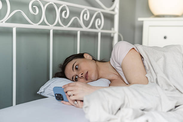 istock Woman lying in bed looking at her smartphone with a thoughtful expression 2206698988