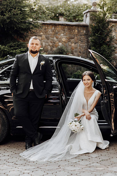 istock A bride and groom pose in front of a black car 2206699678