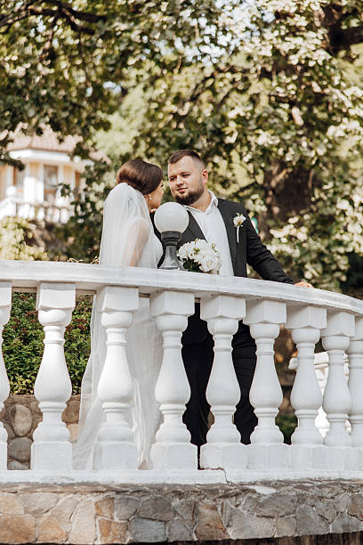 istock A bride and groom are standing on a white railing, looking at each other 2206699685