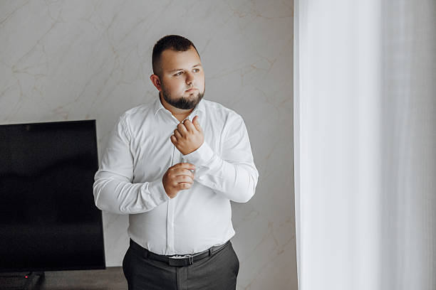 istock A man in a white shirt is getting dressed in front of a window 2206699781